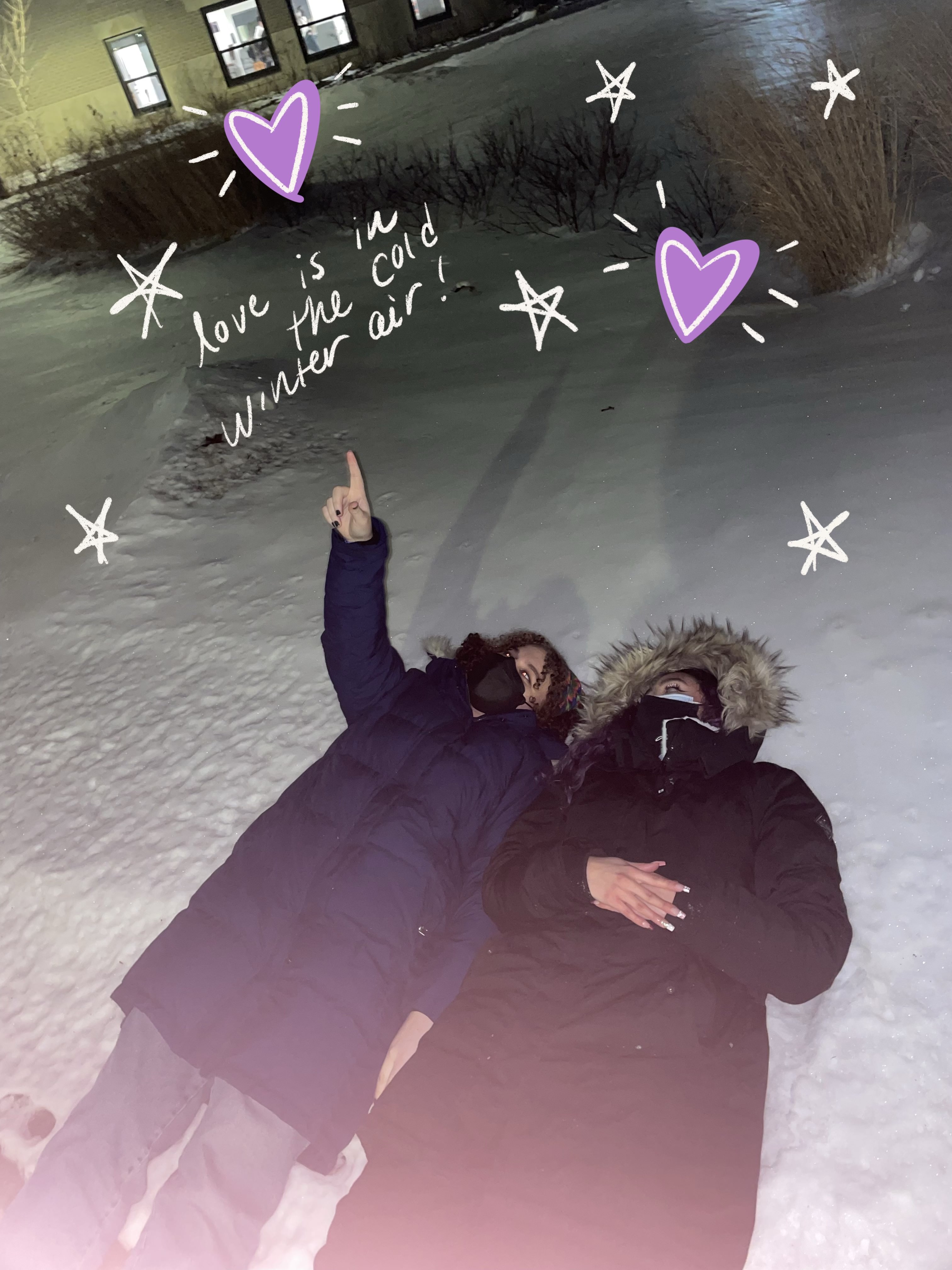 Two people lying in the snow, pointing at the sky.